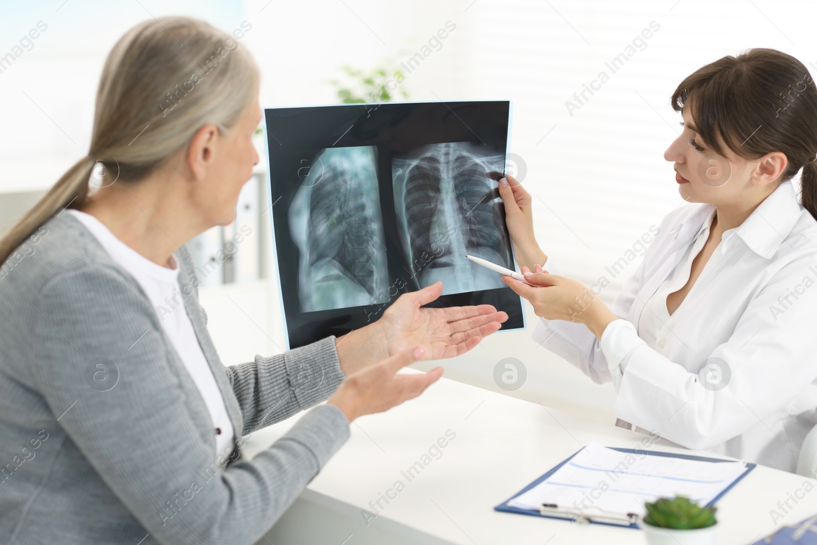 Photo of Lung disease. Doctor showing chest x-ray to her patient at table in clinic