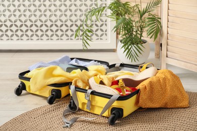 Photo of Open suitcase with traveler's belongings on floor indoors