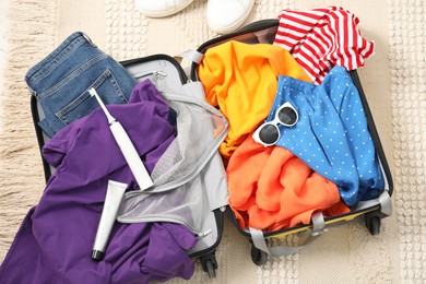 Open suitcase with traveler's belongings on floor, flat lay