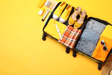 Photo of Open suitcase with traveler's belongings on yellow background, flat lay. Space for text