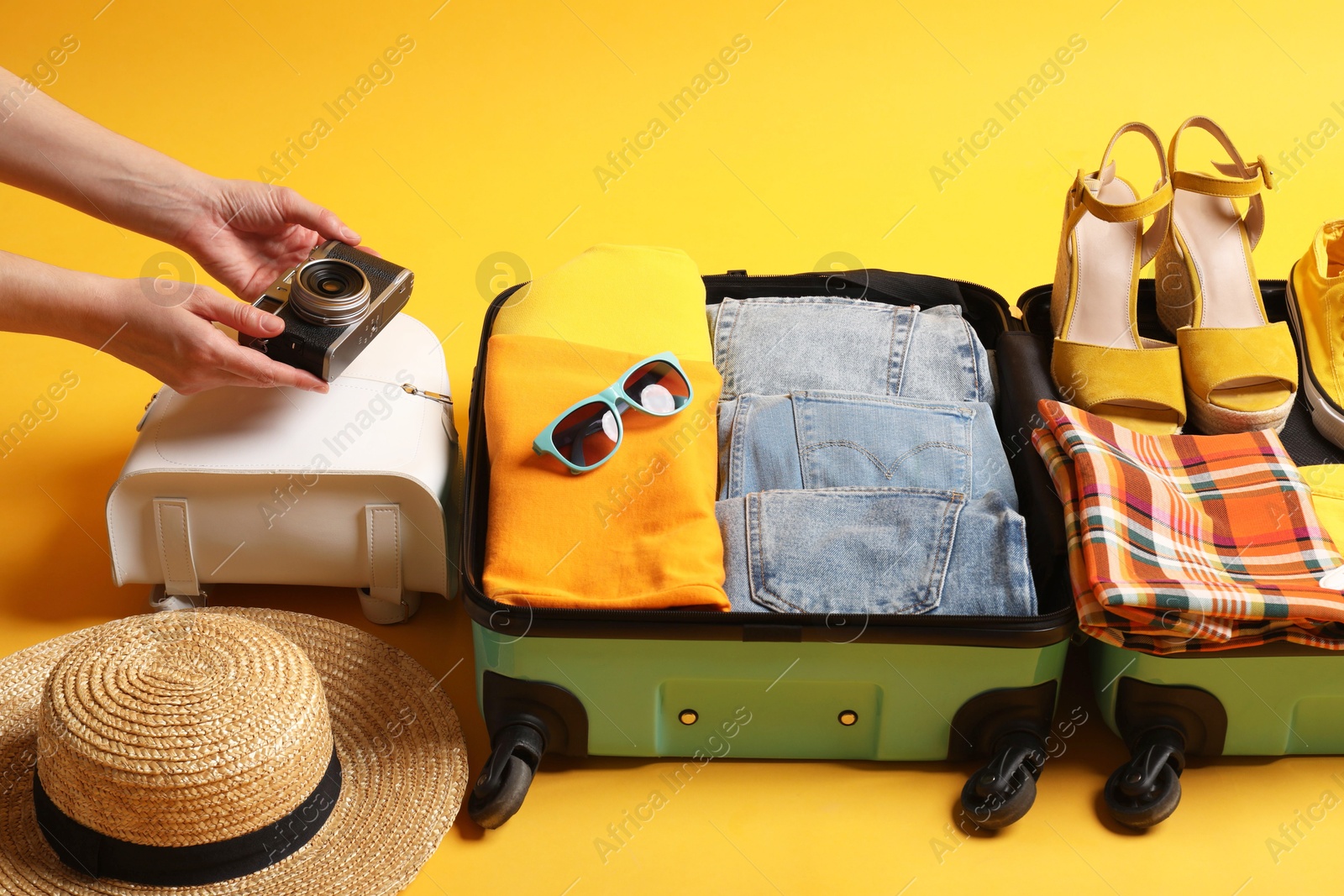 Photo of Woman packing suitcase for trip on yellow background, closeup