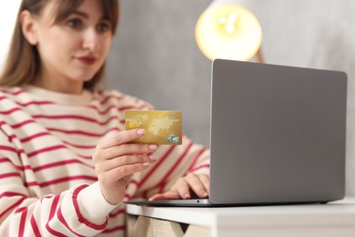 Photo of Online banking. Woman with credit card and laptop paying purchase at table indoors, selective focus
