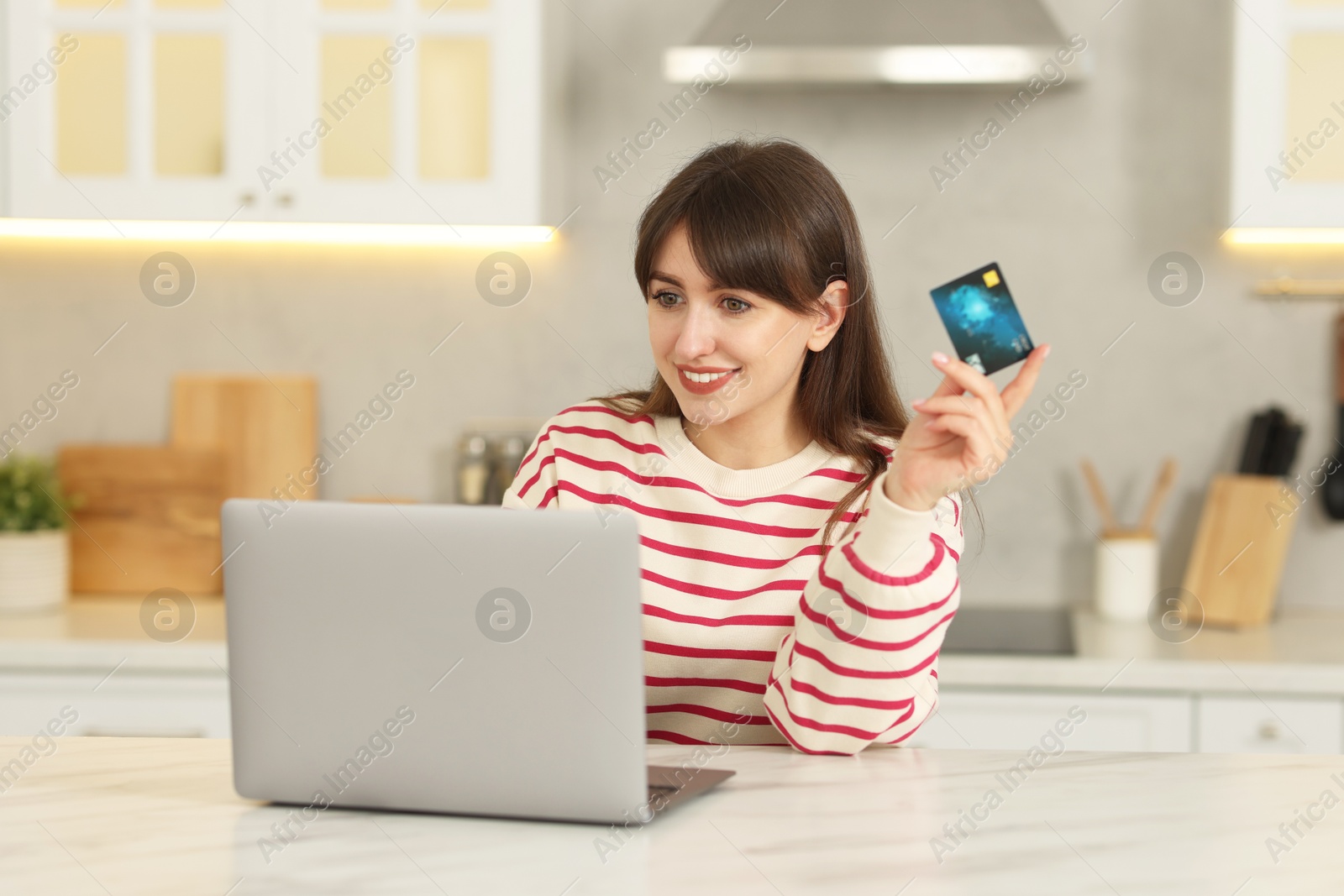 Photo of Online banking. Smiling woman with credit card and laptop paying purchase at table indoors