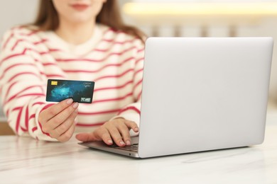 Photo of Online banking. Woman with credit card and laptop paying purchase at white marble table, closeup