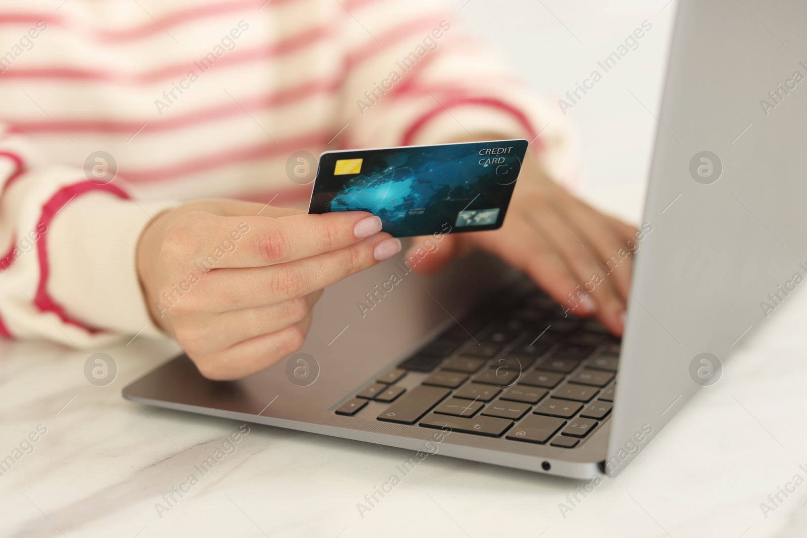 Photo of Online banking. Woman with credit card and laptop paying purchase at white marble table, closeup