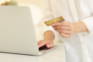 Online banking. Woman with credit card and laptop paying purchase at white table, closeup