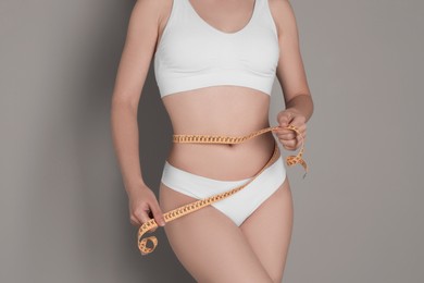 Photo of Woman with measuring tape showing her slim body against grey background, closeup