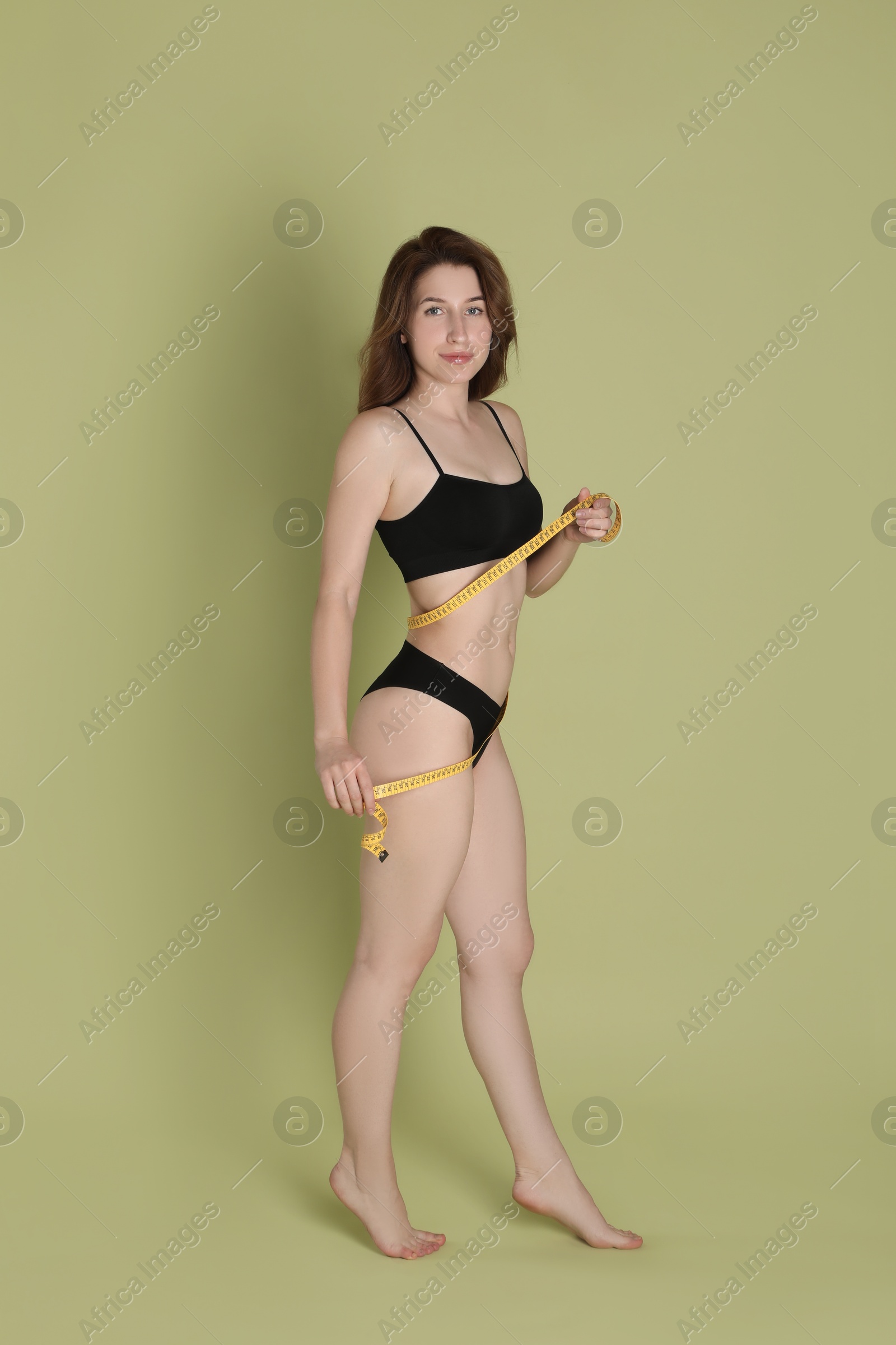 Photo of Woman with measuring tape showing her slim body against olive background