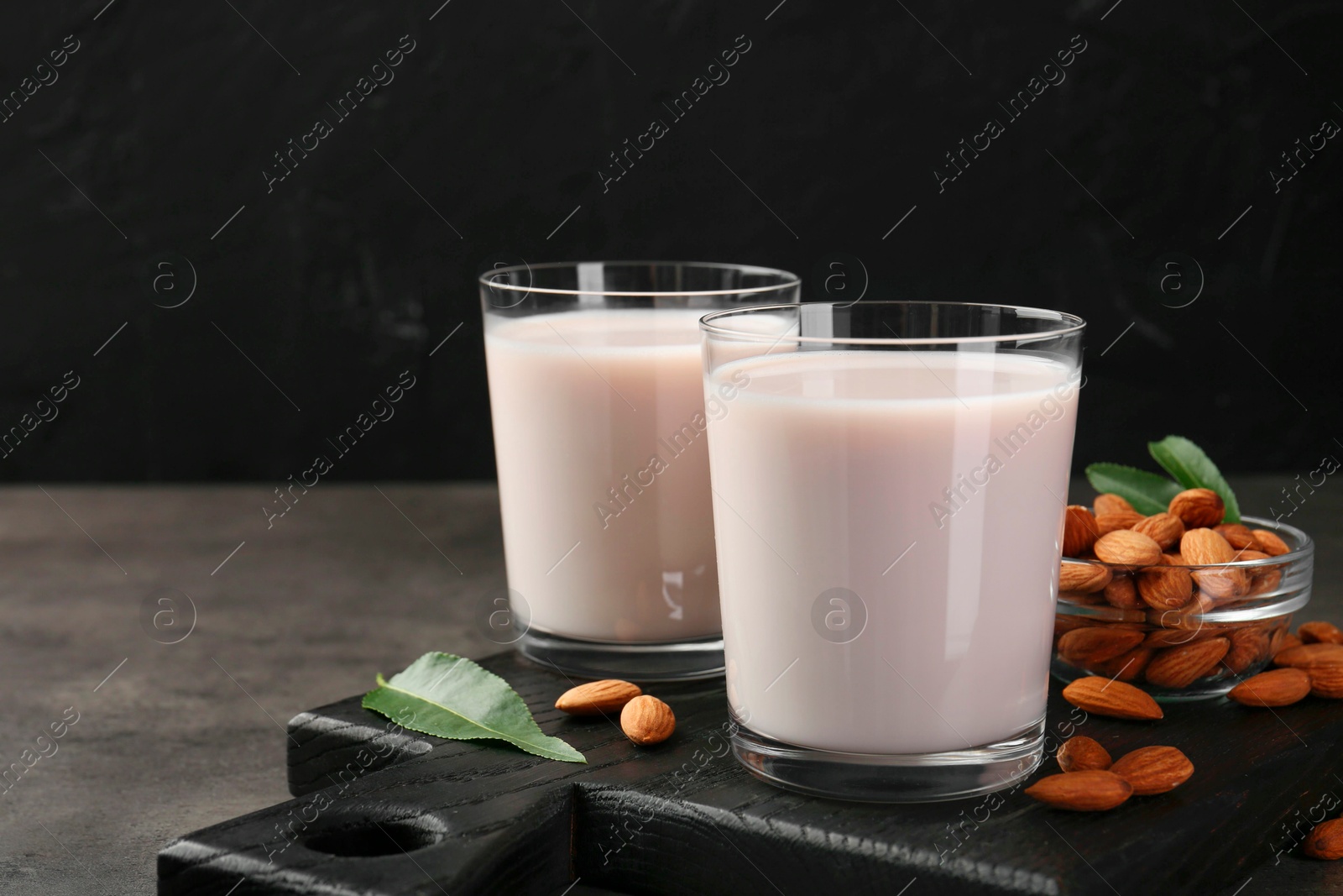 Photo of Glasses of almond milk and almonds on grey table