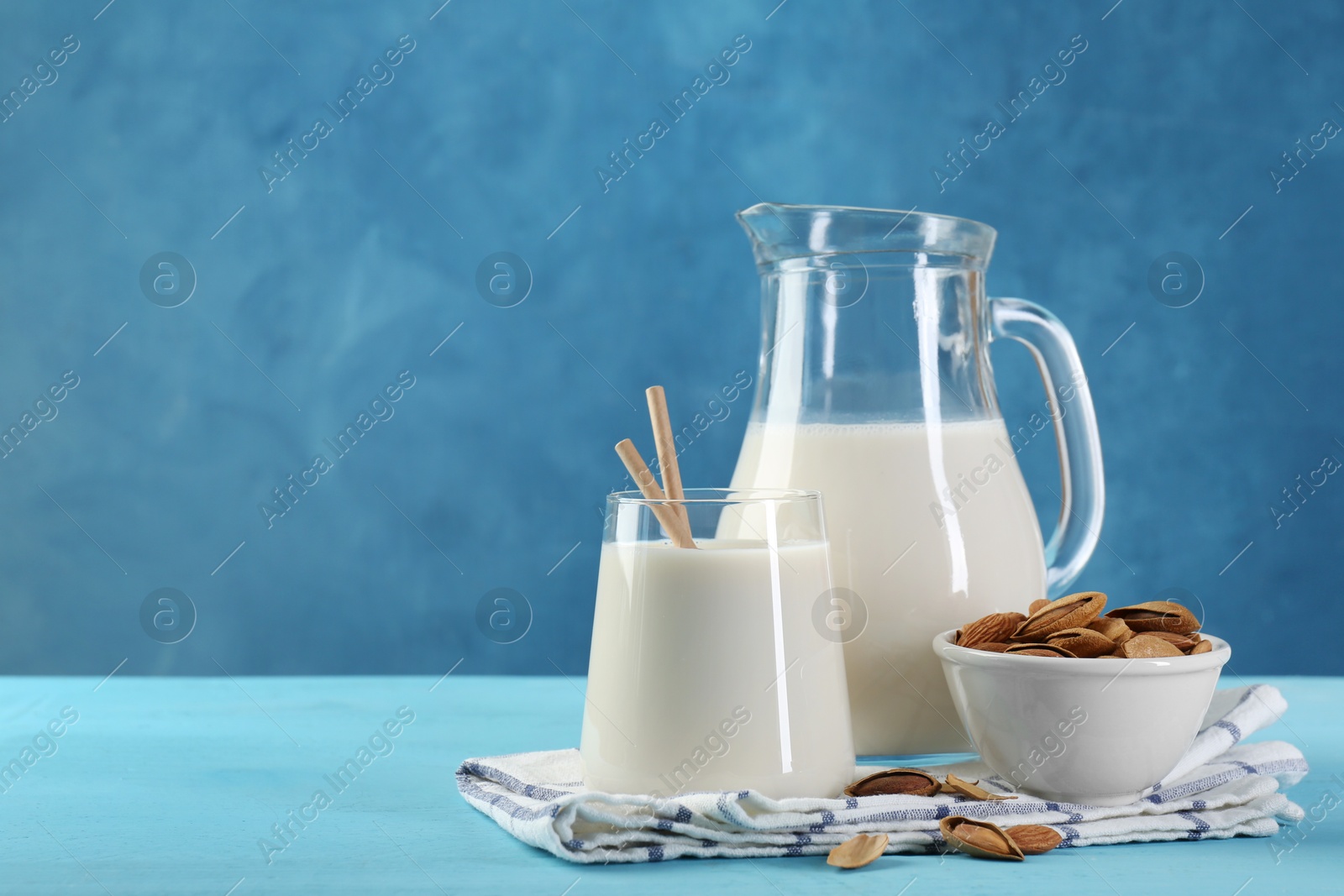 Photo of Glass of almond milk, jug and almonds on light blue wooden table, space for text