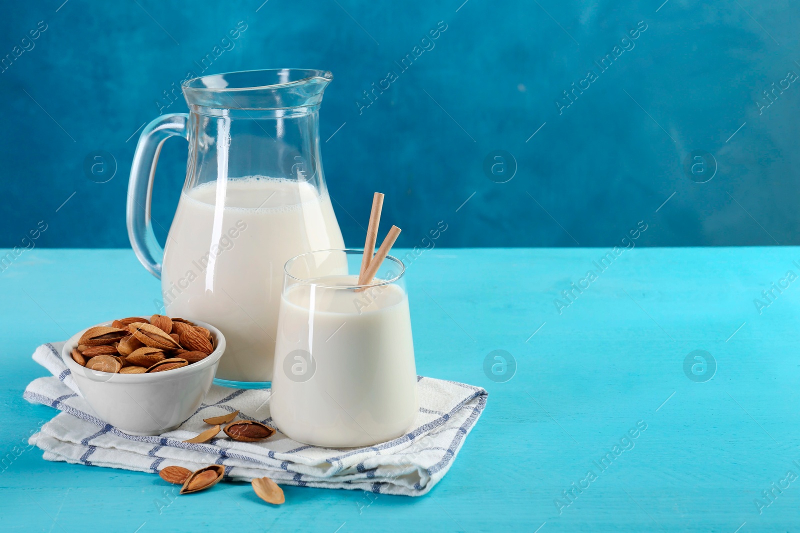 Photo of Glass of almond milk, jug and almonds on light blue wooden table, space for text