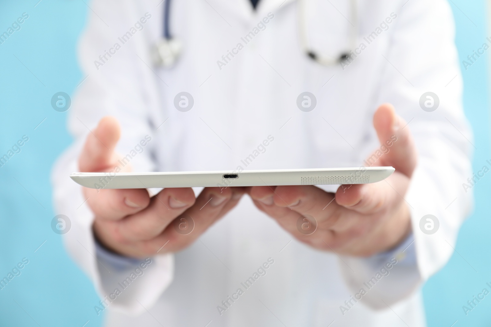 Photo of Doctor with tablet on light blue background, selective focus