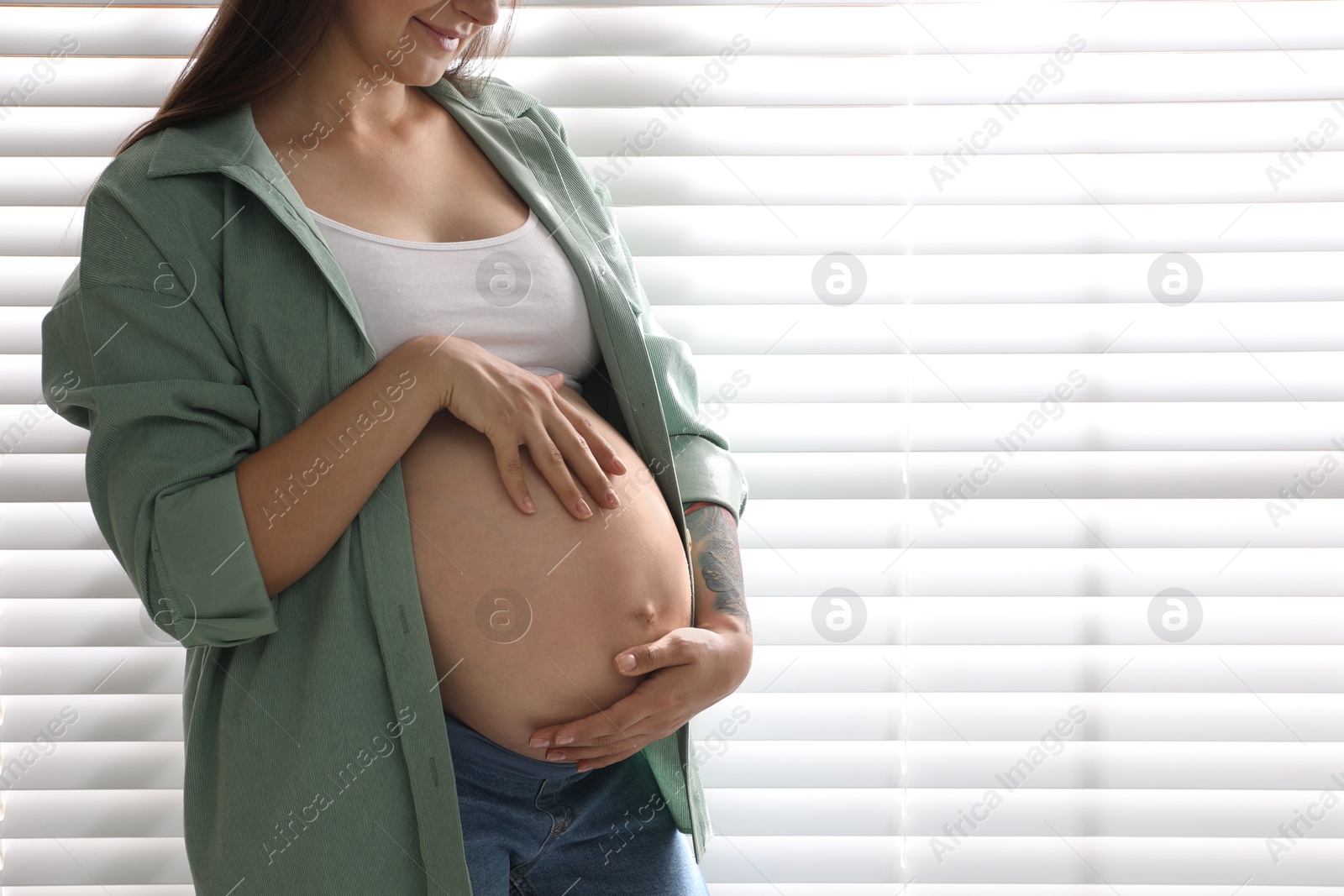 Photo of Beautiful pregnant woman near window blinds at home, closeup. Space for text