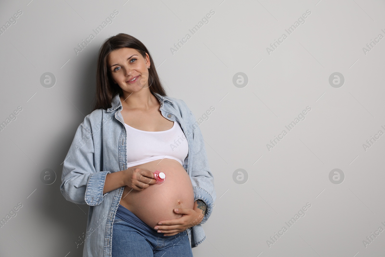 Photo of Pregnant woman with pink pacifier on gray background, space for text