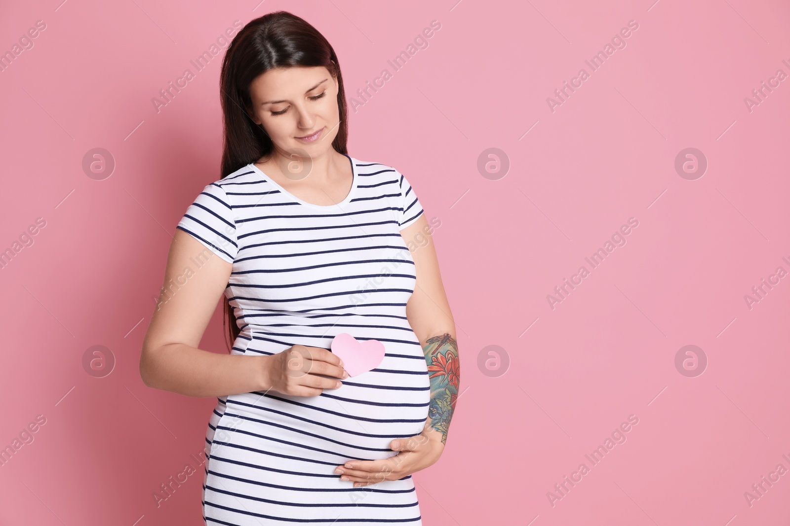 Photo of Beautiful pregnant woman with paper heart on pink background, space for text