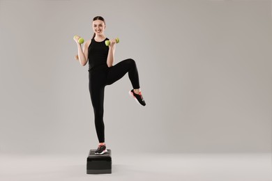 Photo of Young woman doing aerobic exercise with dumbbells and step platform on light background. Space for text