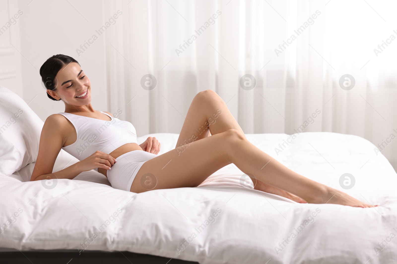 Photo of Smiling woman with perfect skin in underwear on bed. Body care