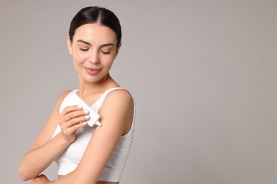 Photo of Beautiful woman applying cream onto arm on grey background, space for text. Body care