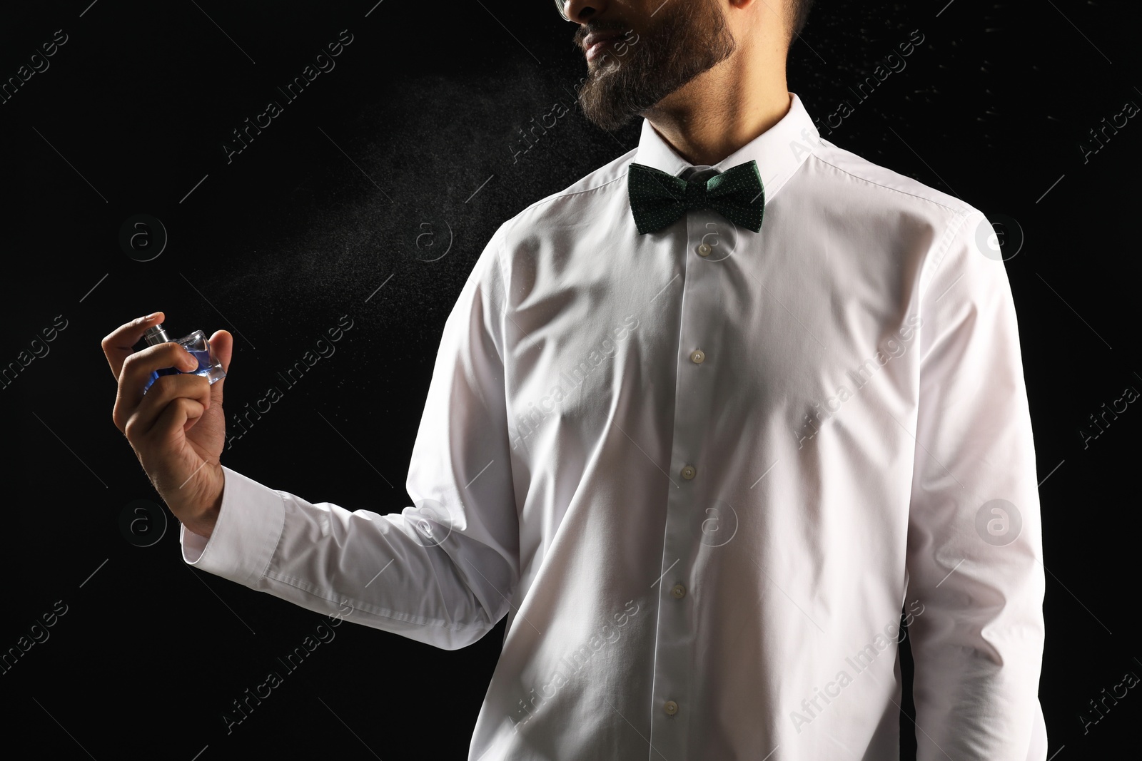 Photo of Man spraying luxury perfume on dark background, closeup