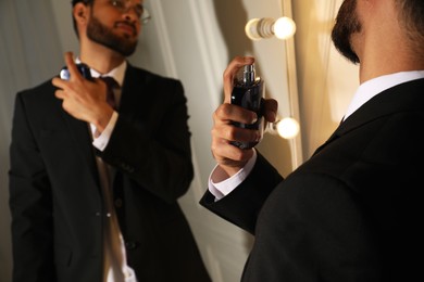 Photo of Man spraying luxury perfume near mirror indoors, closeup