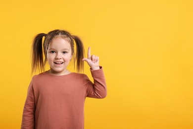 Photo of Cute little girl pointing at something on orange background, space for text