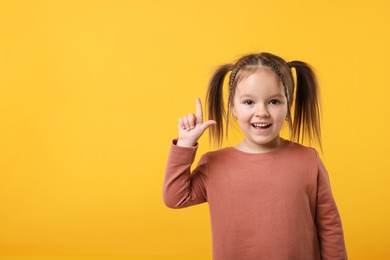 Photo of Cute little girl pointing at something on orange background, space for text