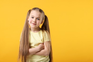 Photo of Portrait of cute little girl with crossed arms on orange background, space for text