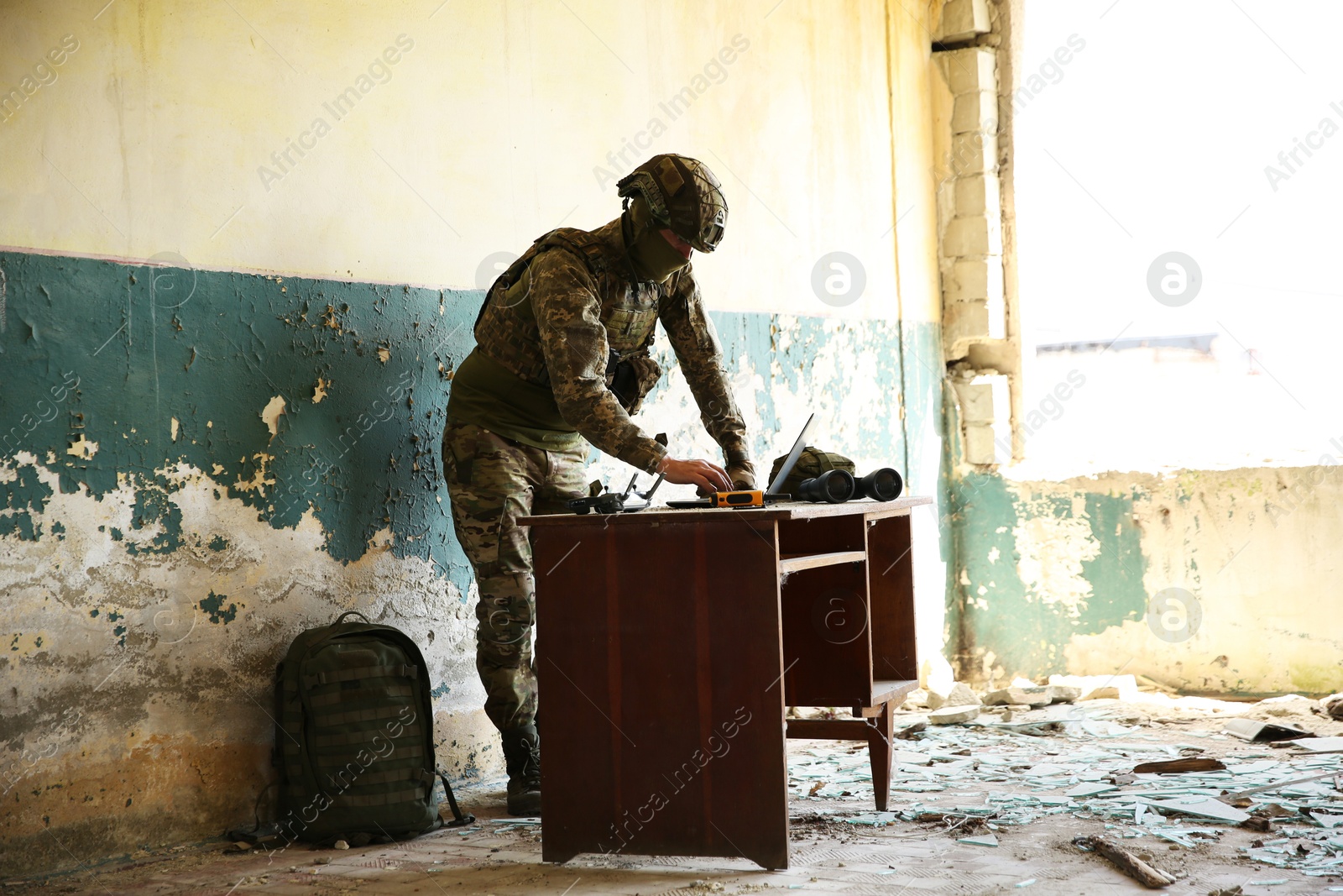 Photo of Military mission. Soldier in uniform using laptop at table inside abandoned building