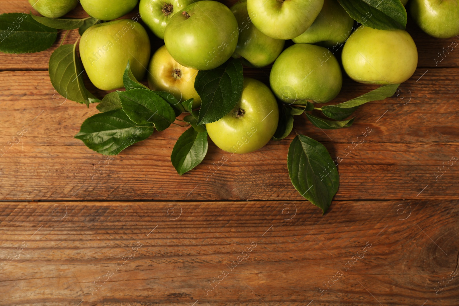 Photo of Ripe green apples with leaves on wooden table, flat lay. Space for text