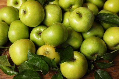 Photo of Fresh ripe green apples with leaves on wooden table, closeup