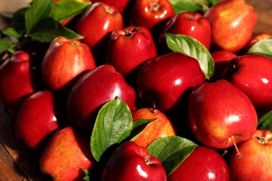 Photo of Fresh ripe red apples with leaves on wooden table, closeup