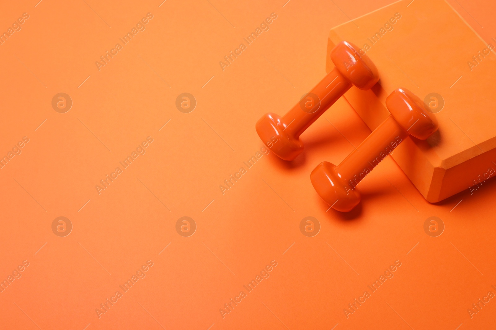 Photo of Dumbbells and yoga block on orange background. Space for text