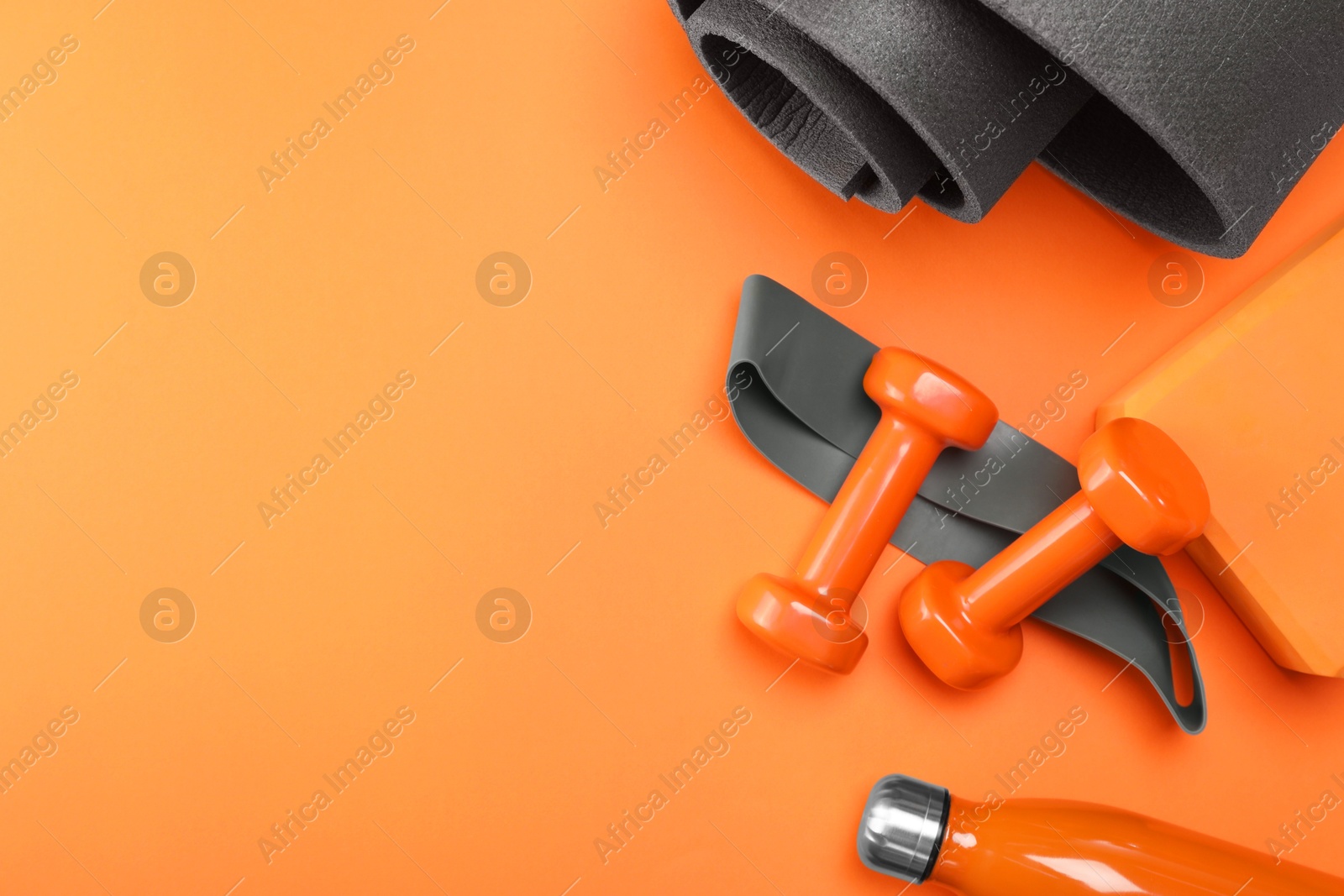 Photo of Dumbbells, yoga block, mat, thermo bottle and fitness elastic band on orange background, flat lay. Space for text