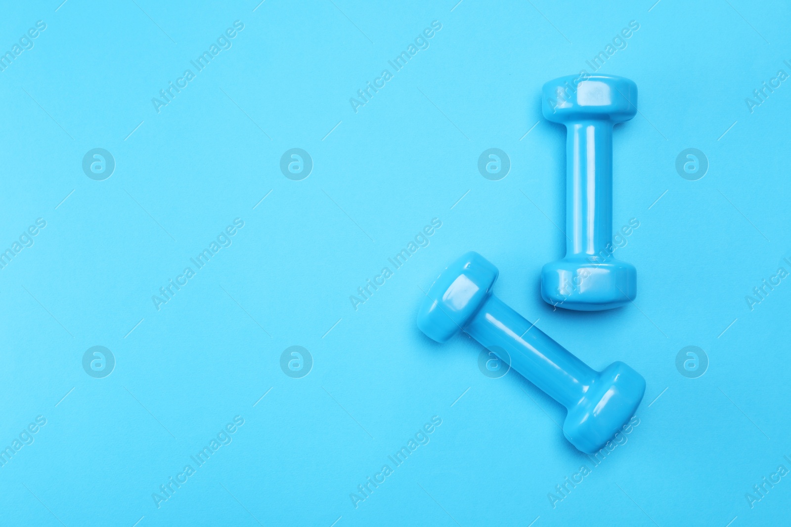 Photo of Two dumbbells on light blue background, top view. Space for text