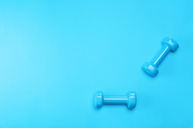 Photo of Two dumbbells on light blue background, top view. Space for text