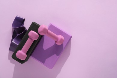 Two dumbbells, yoga blocks and fitness elastic band on violet background, flat lay. Space for text