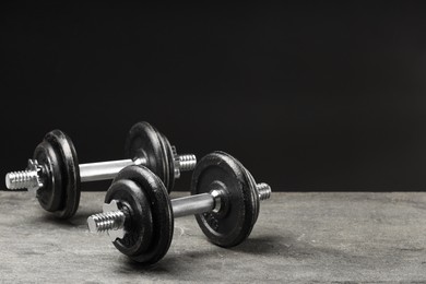 Two barbells on grey textured table, closeup. Space for text