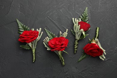 Many stylish red boutonnieres on black table, flat lay