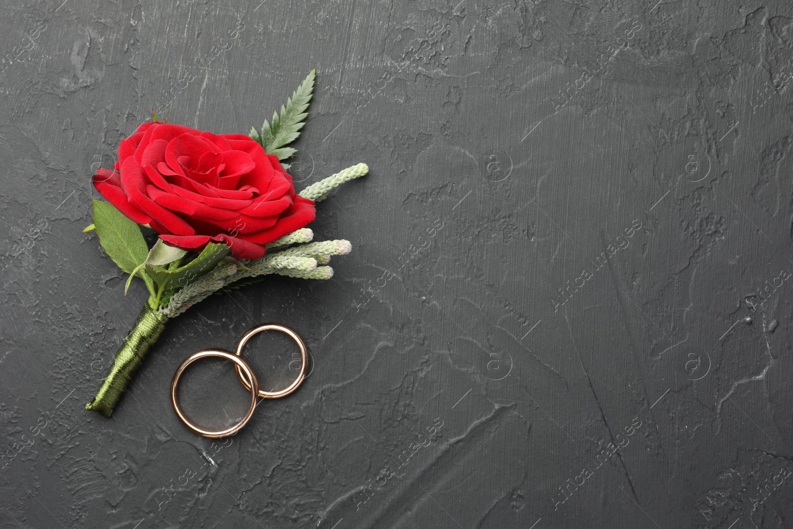 Photo of Stylish red boutonniere and rings on black table, top view. Space for text