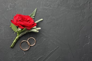 Photo of Stylish red boutonniere and rings on black table, top view. Space for text