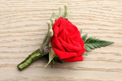 One stylish red boutonniere on light wooden table, top view