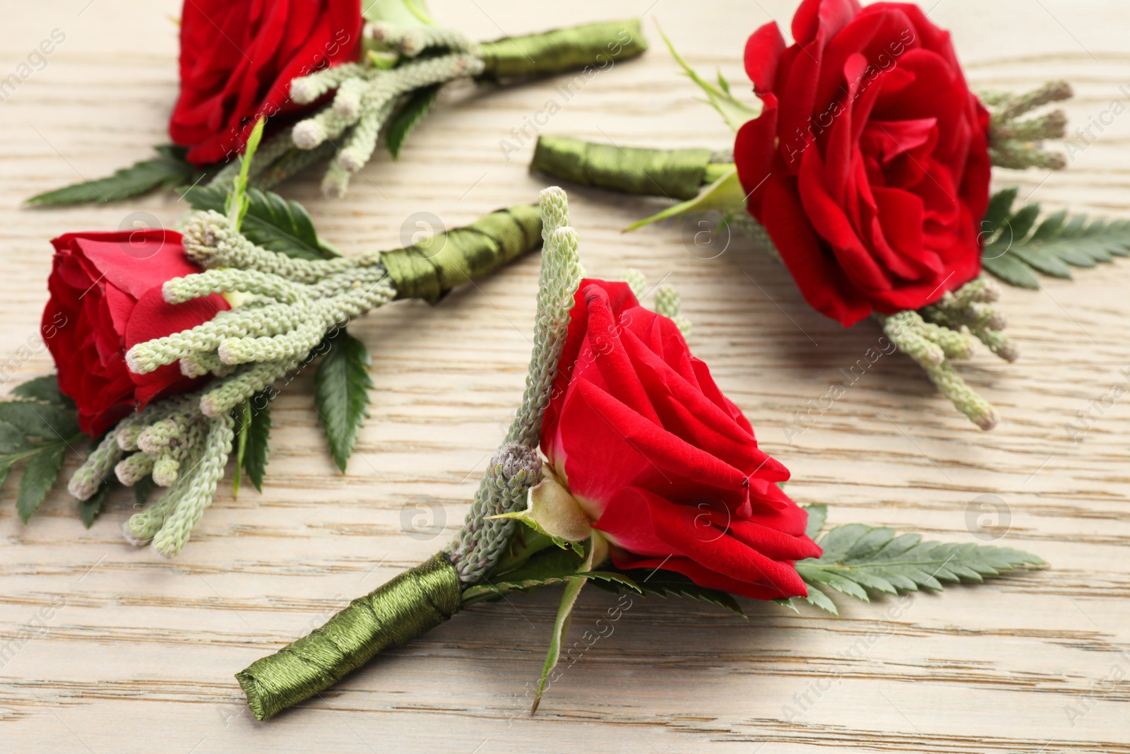 Photo of Many stylish red boutonnieres on light wooden table