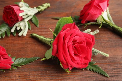 Many stylish red boutonnieres on wooden table