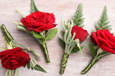 Many stylish red boutonnieres on light wooden table, flat lay