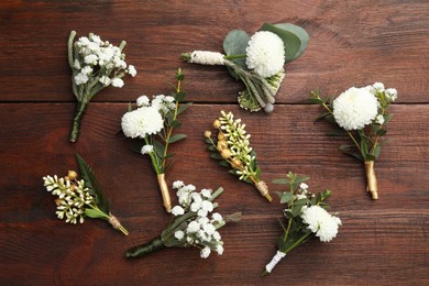 Photo of Small stylish boutonnieres on wooden table, flat lay