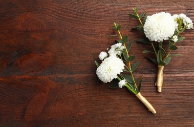 Small stylish boutonnieres on wooden table, top view. Space for text