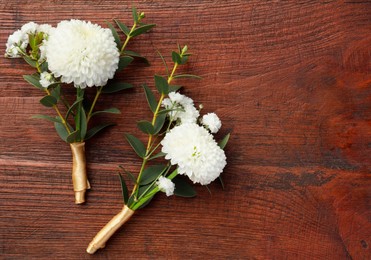 Small stylish boutonnieres on wooden table, top view. Space for text