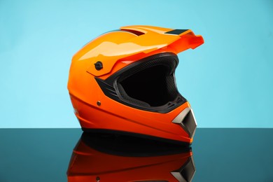 Photo of Modern motorcycle helmet with visor on mirror surface against light blue background