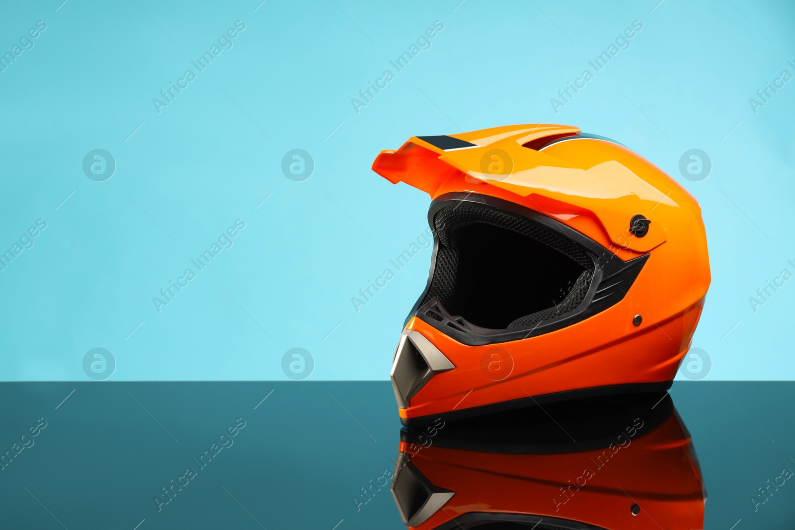 Photo of Modern motorcycle helmet with visor on mirror surface against light blue background. Space for text