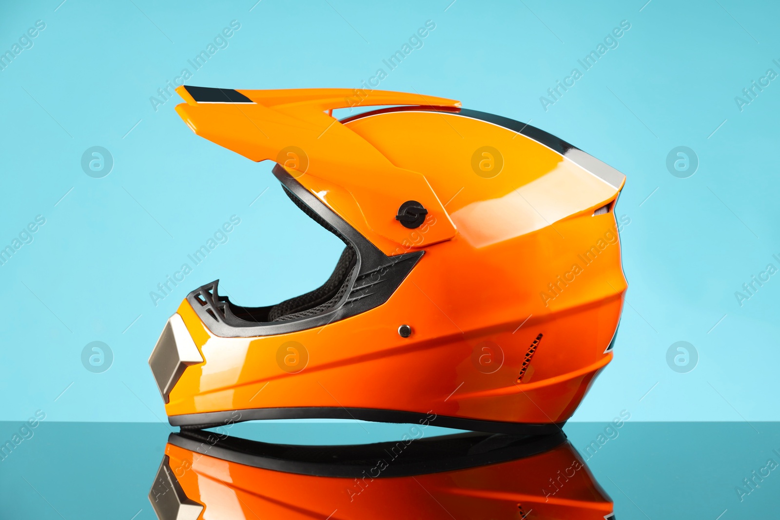 Photo of Modern motorcycle helmet with visor on mirror surface against light blue background